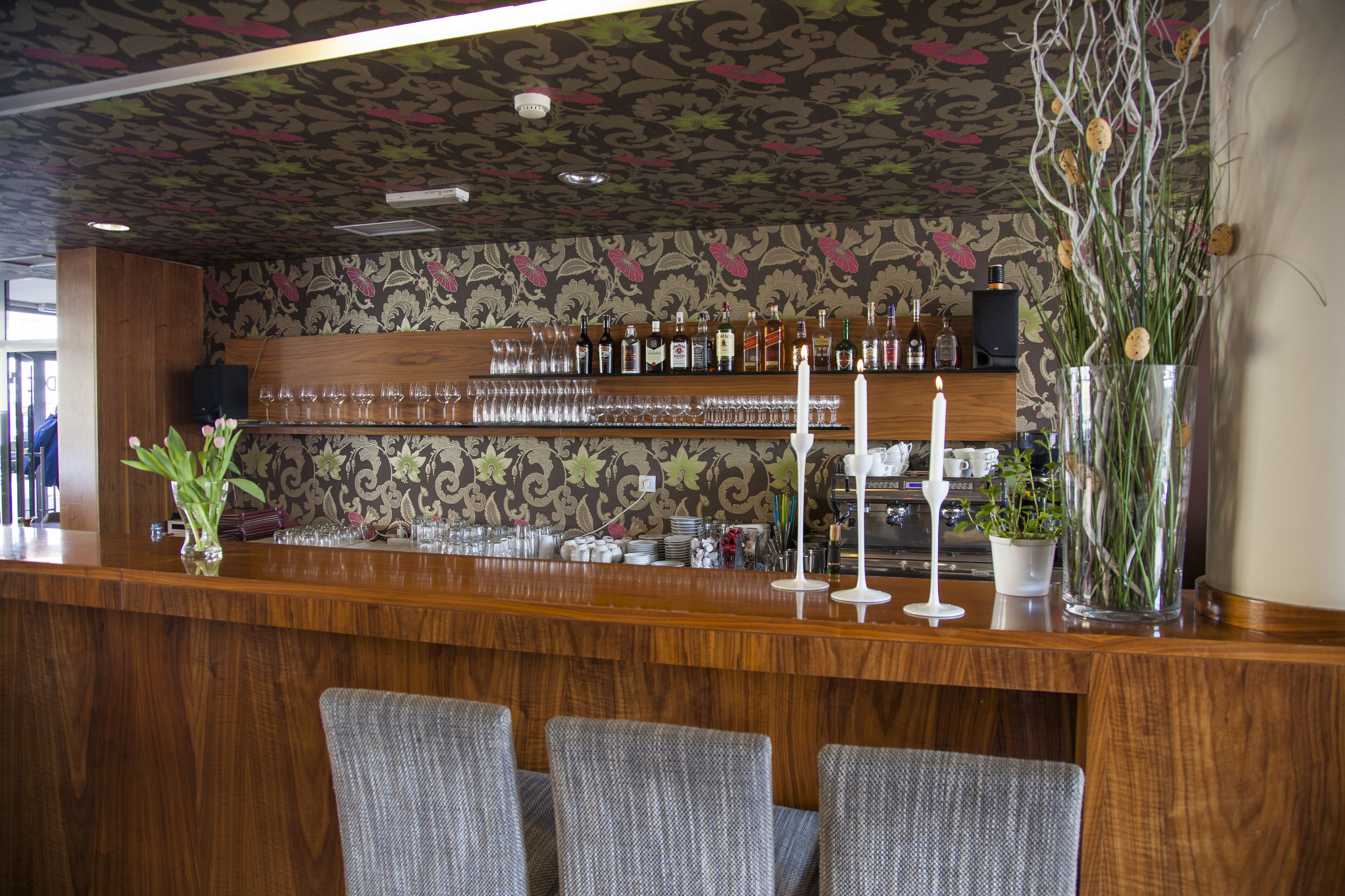 Un espace bar avec un comptoir en bois, des tabourets de bar et un mur orné d’un motif floral.