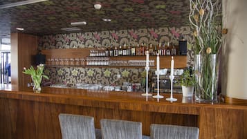 A bar area with wooden counter, bar stools, and a floral patterned wall.