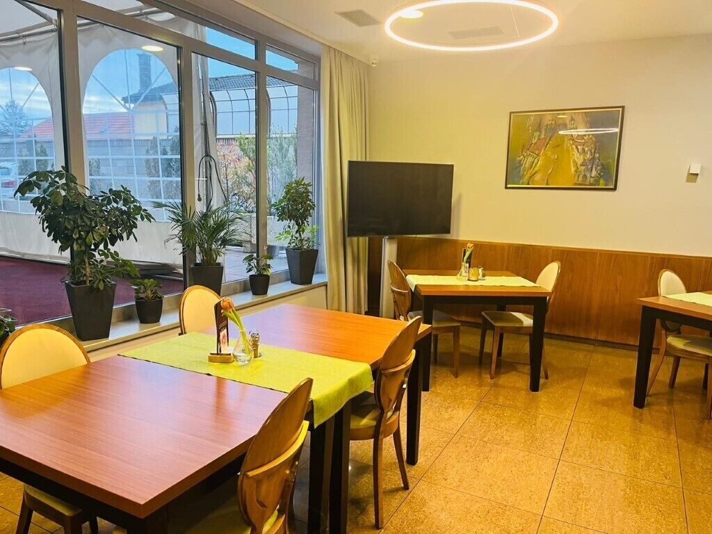Un comedor con mesas, sillas, plantas en macetas, un televisor de pantalla plana y un cuadro en la pared.
