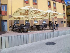 Mobiliario exterior con sombrillas, un camino pavimentado y un edificio con varias ventanas y balcones.