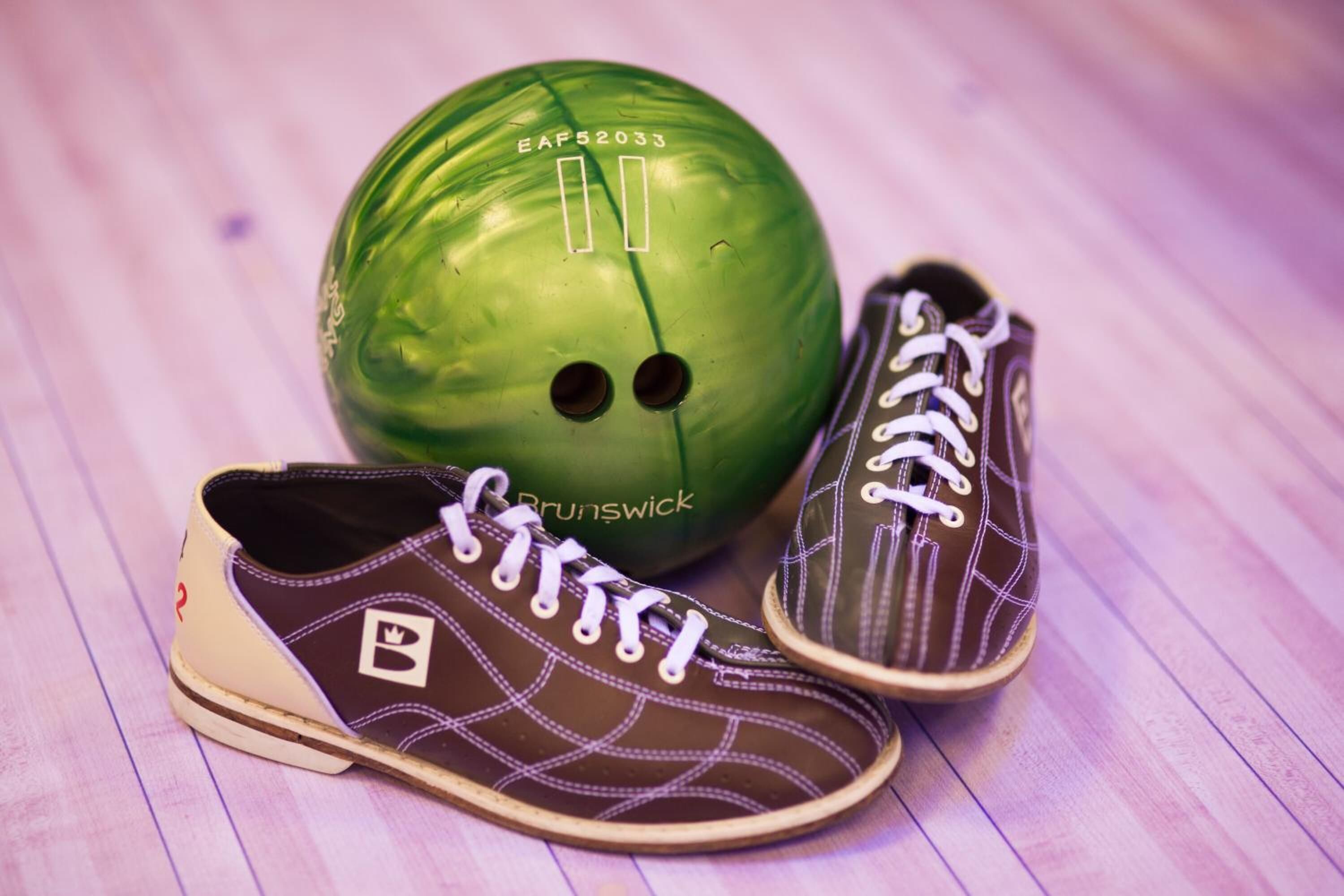 Una bola de boliche verde y dos zapatos sobre un piso de madera.
