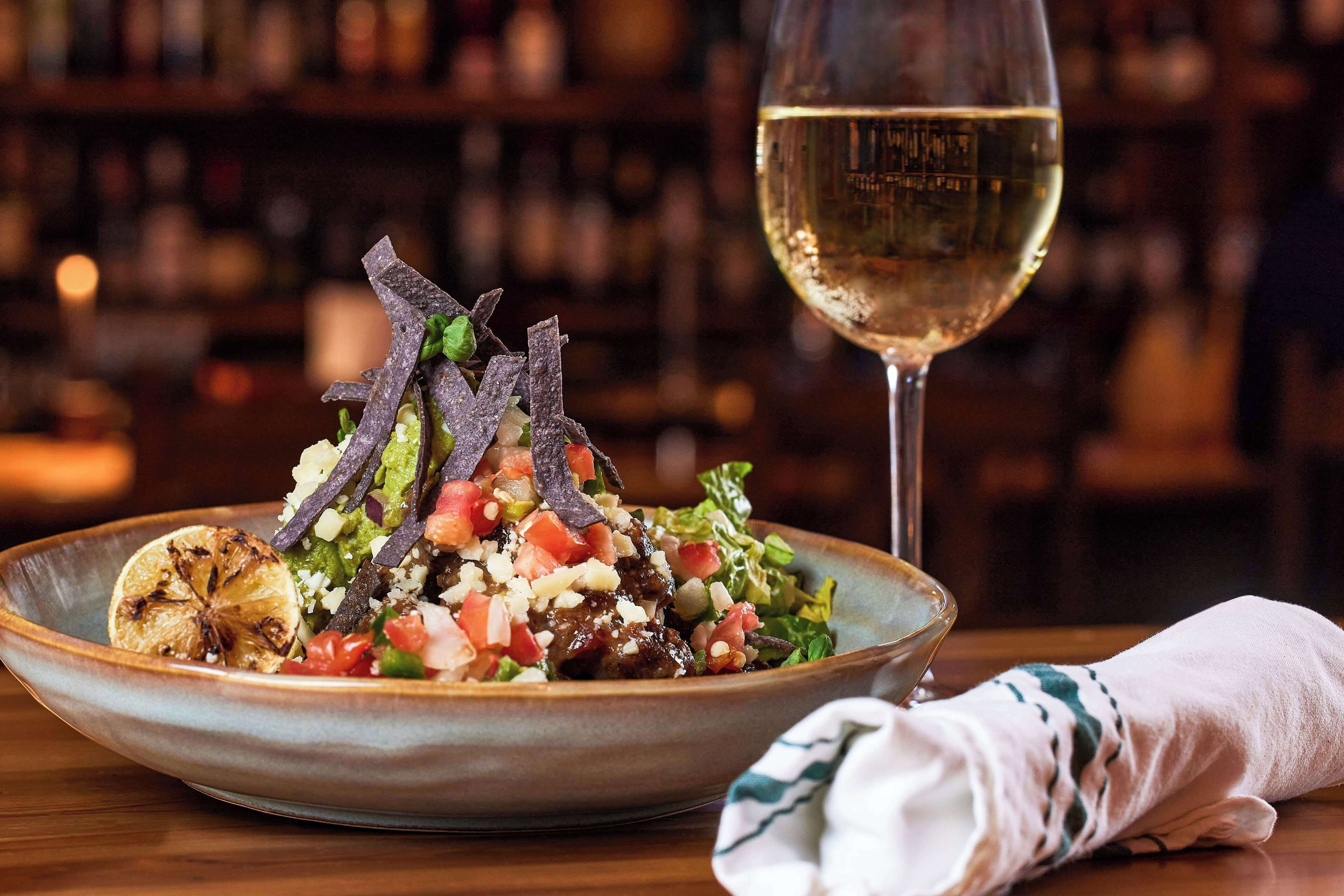 Un tazón de ensalada con una copa de vino blanco sobre una mesa.