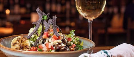 Un tazón de ensalada con una copa de vino blanco sobre una mesa.