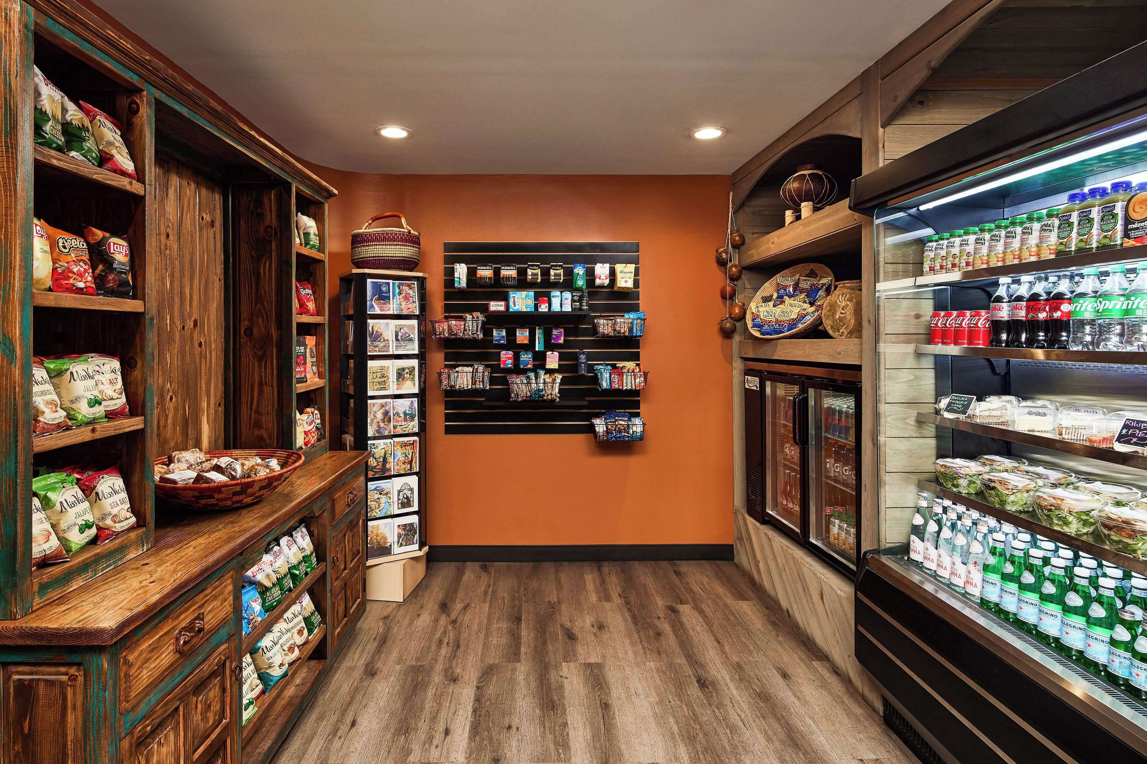 A grocery store interior with wooden shelves stocked with various products, a central display wall, and a refrigerated section on the right.