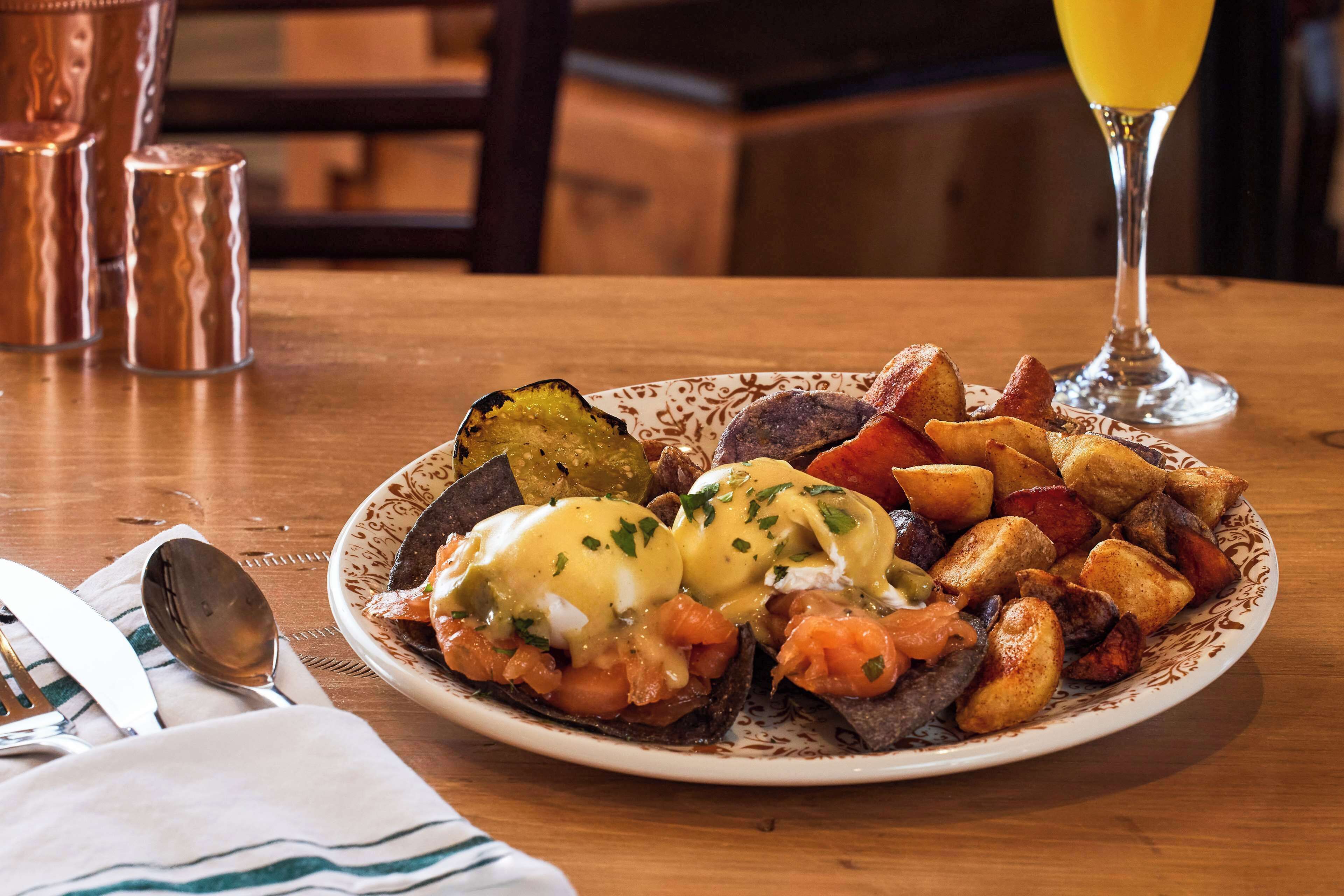 A breakfast plate with eggs benedict, potatoes, and vegetables on a table.