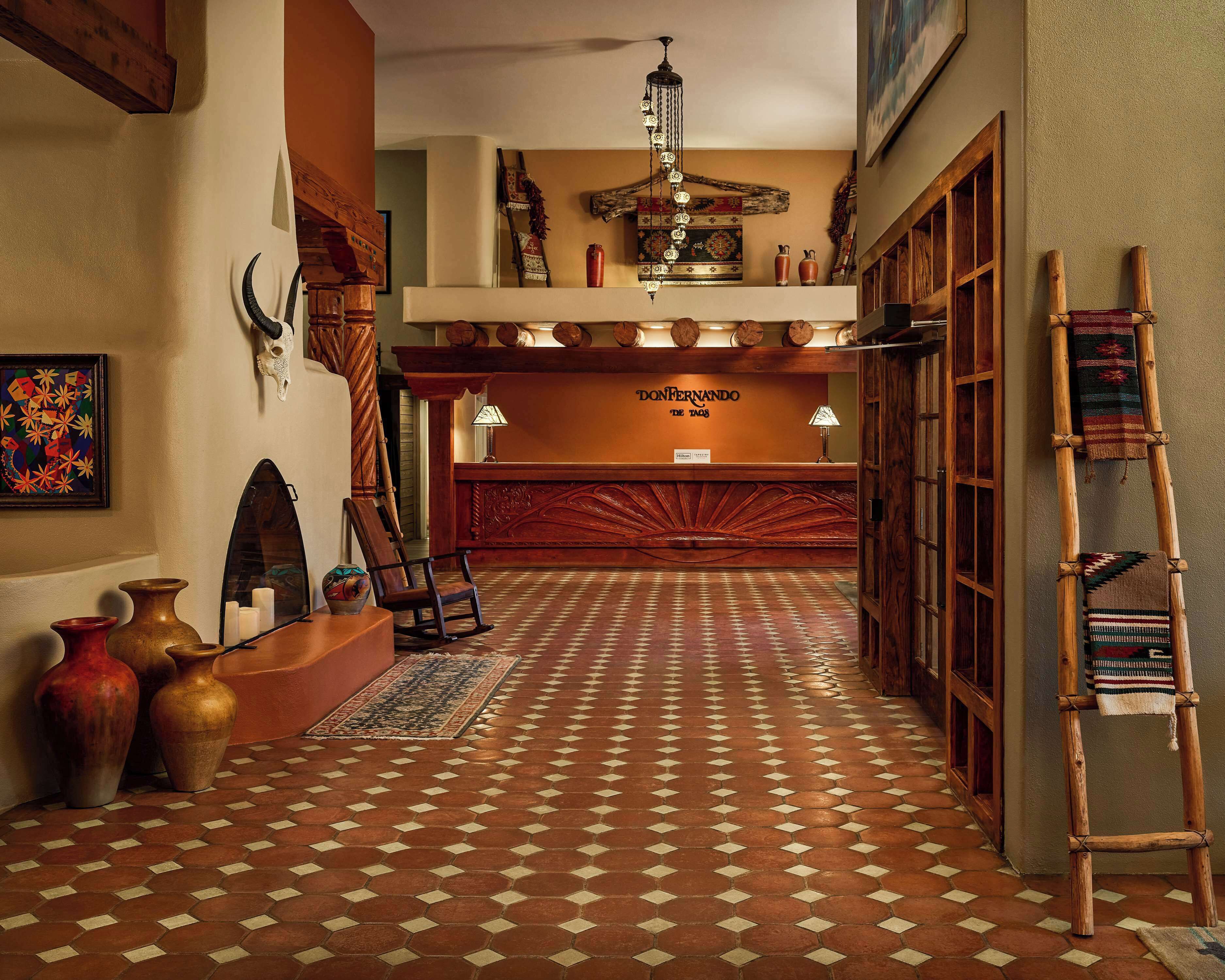 A hotel lobby with a patterned floor, wooden reception desk, and traditional decor including vases and a ladder.