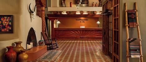 A hotel lobby with a patterned floor, wooden reception desk, and traditional decor including vases and a ladder.