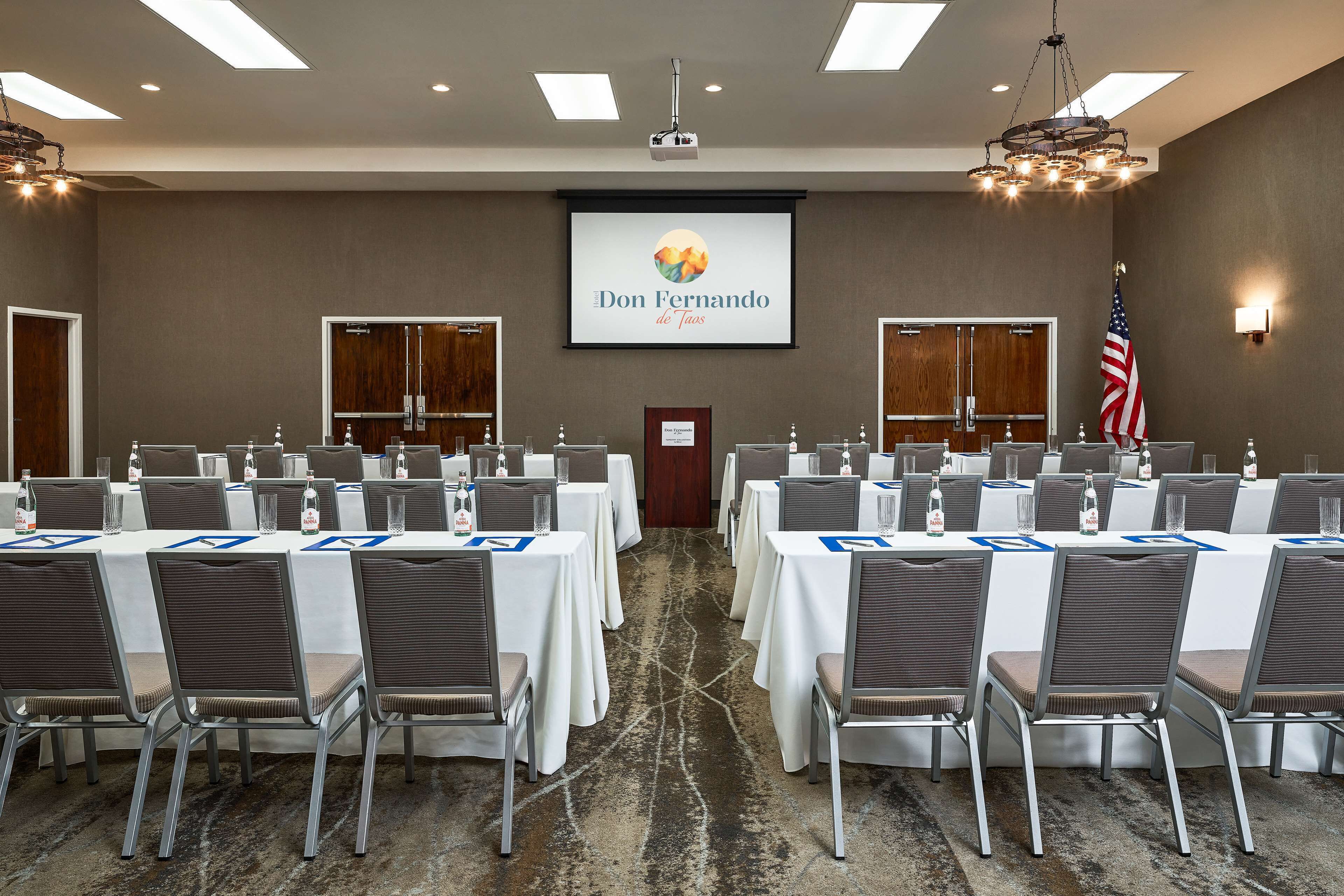 A conference room with multiple tables, chairs, and a projector screen displaying "Don Fernando de Taos".