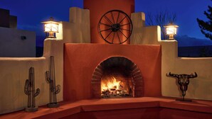Una chimenea de piedra con fuego, rodeada por un muro bajo y dos faroles de pared.