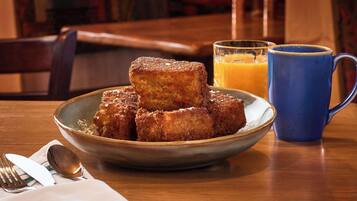 A plate of French toast with syrup, a blue mug, and a glass of orange juice on a wooden table.