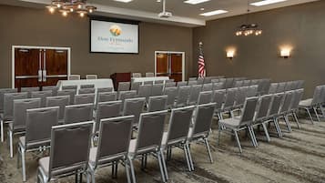 A conference room with rows of chairs, a podium, a projector screen, and an American flag.