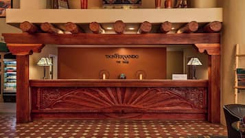 Un mostrador de recepción con detalles de madera tallada, una zona de registro y un suelo de baldosas.