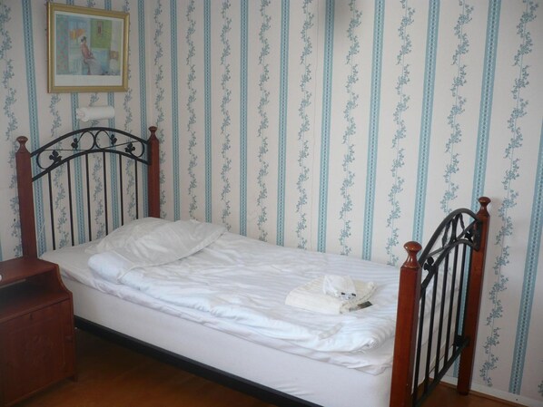 Un lit simple avec une tête de lit et un pied de lit en bois, une table de chevet en bois et un tableau encadré accroché au mur.
