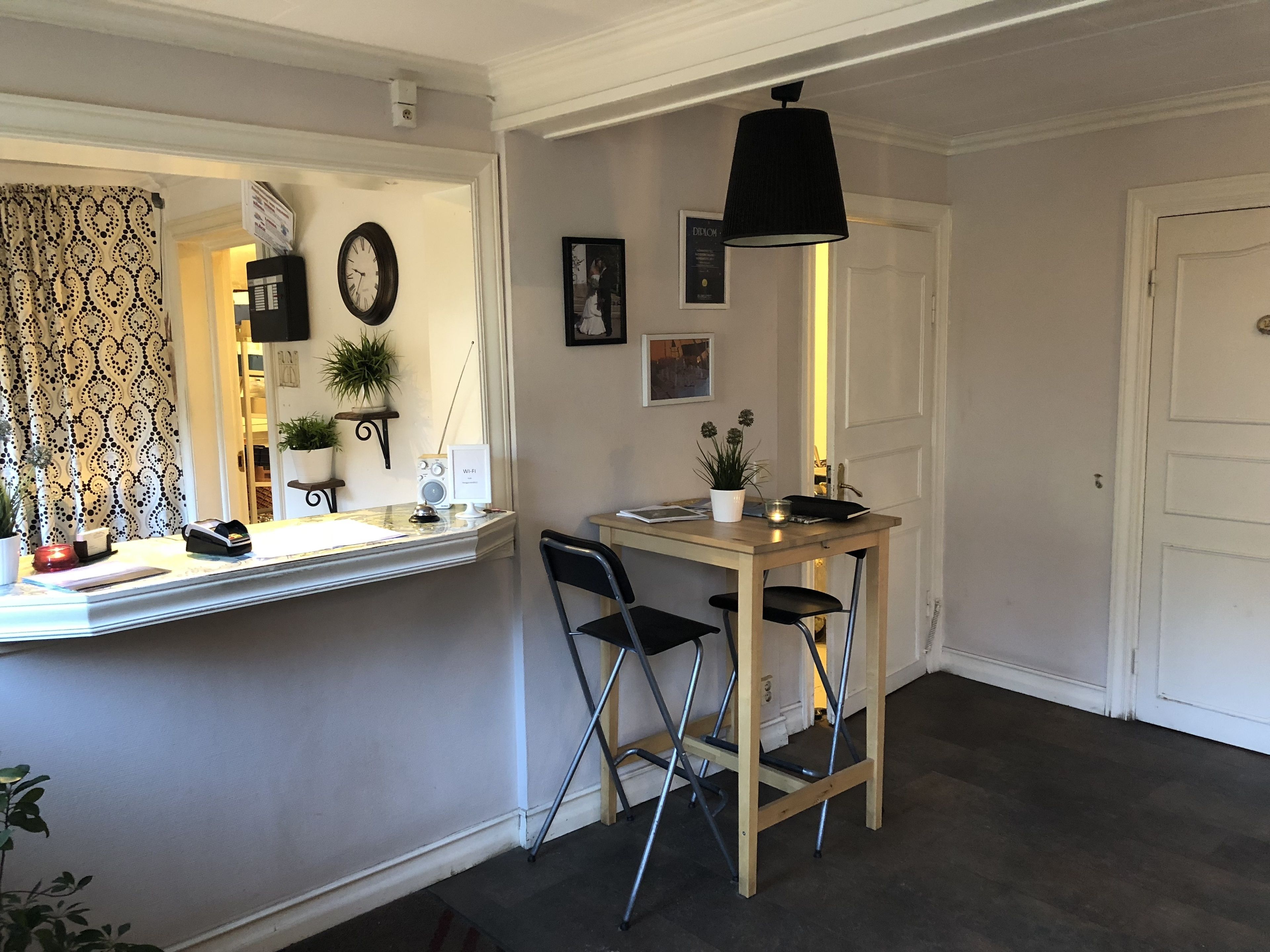A compact room with a desk, two chairs, a small table, a wall clock, a potted plant, and a door.