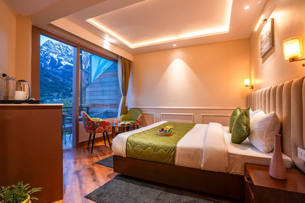 Una habitación de hotel con cama, escritorio, silla y vistas a las montañas desde la ventana.