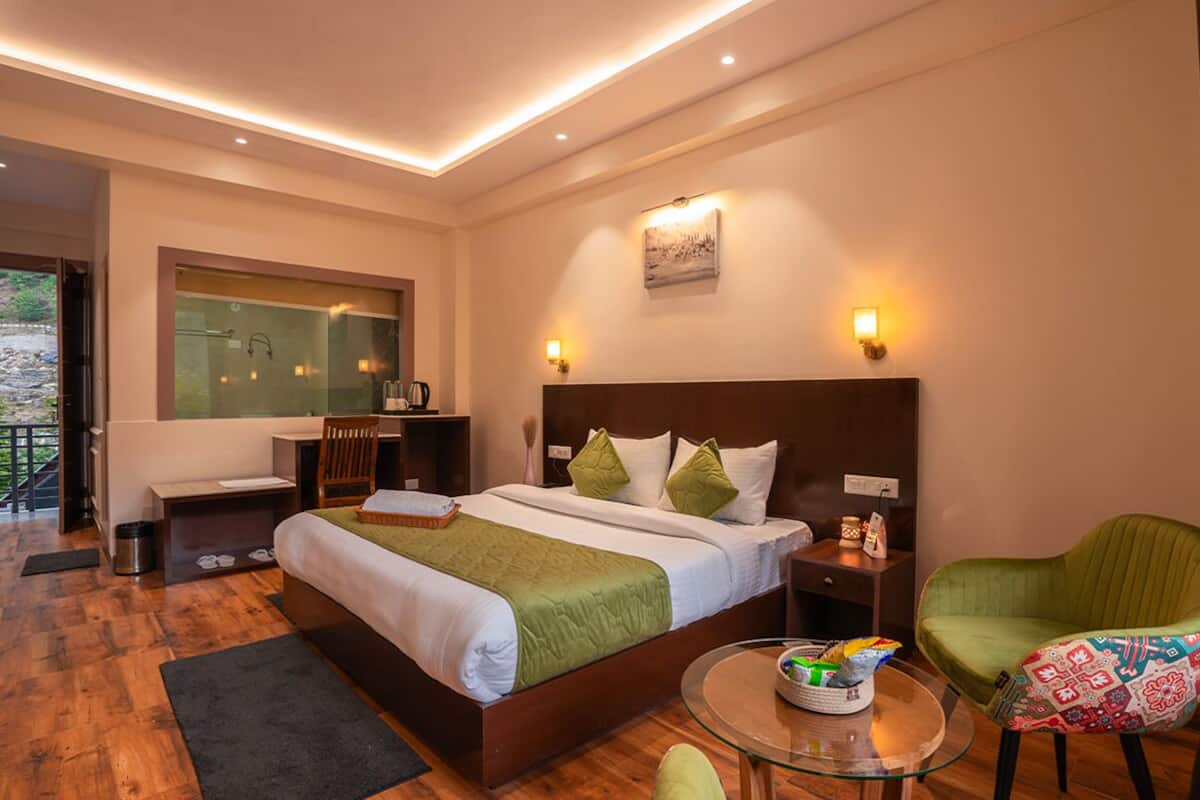 Una habitación de hotel moderna con una cama grande, una mesita de centro de vidrio, un sillón verde y un escritorio con una silla.