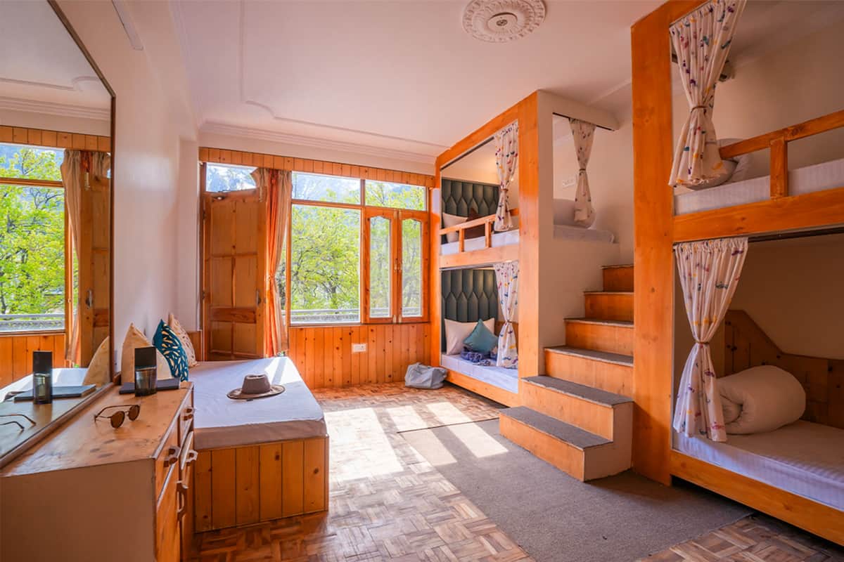 Una cabaña acogedora con interior de madera, una litera, un escritorio con silla y ventanas amplias que dan a vista de árboles.