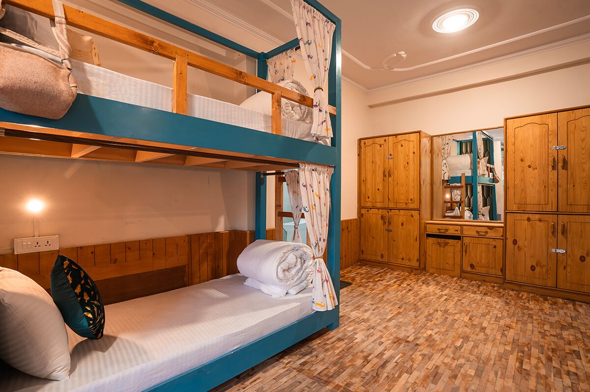 A bunk bed room with wooden headboard, a single bed, a wardrobe, and a mirror.