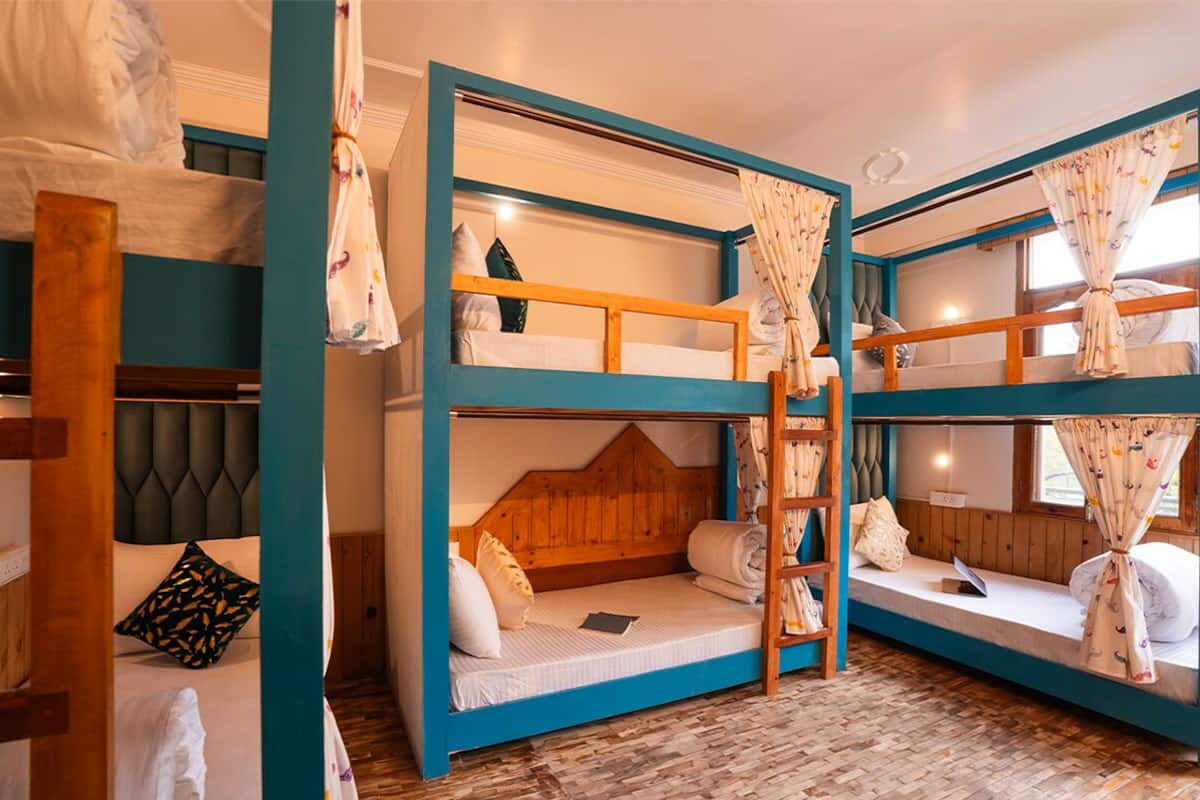 Una habitación con literas, cabeceros de madera y una ventana con cortinas.