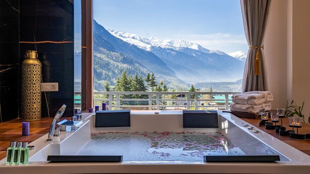 A bathroom with a large bathtub, a view of snow-capped mountains, and a balcony with towels. -  Moustache Manali (Manali)