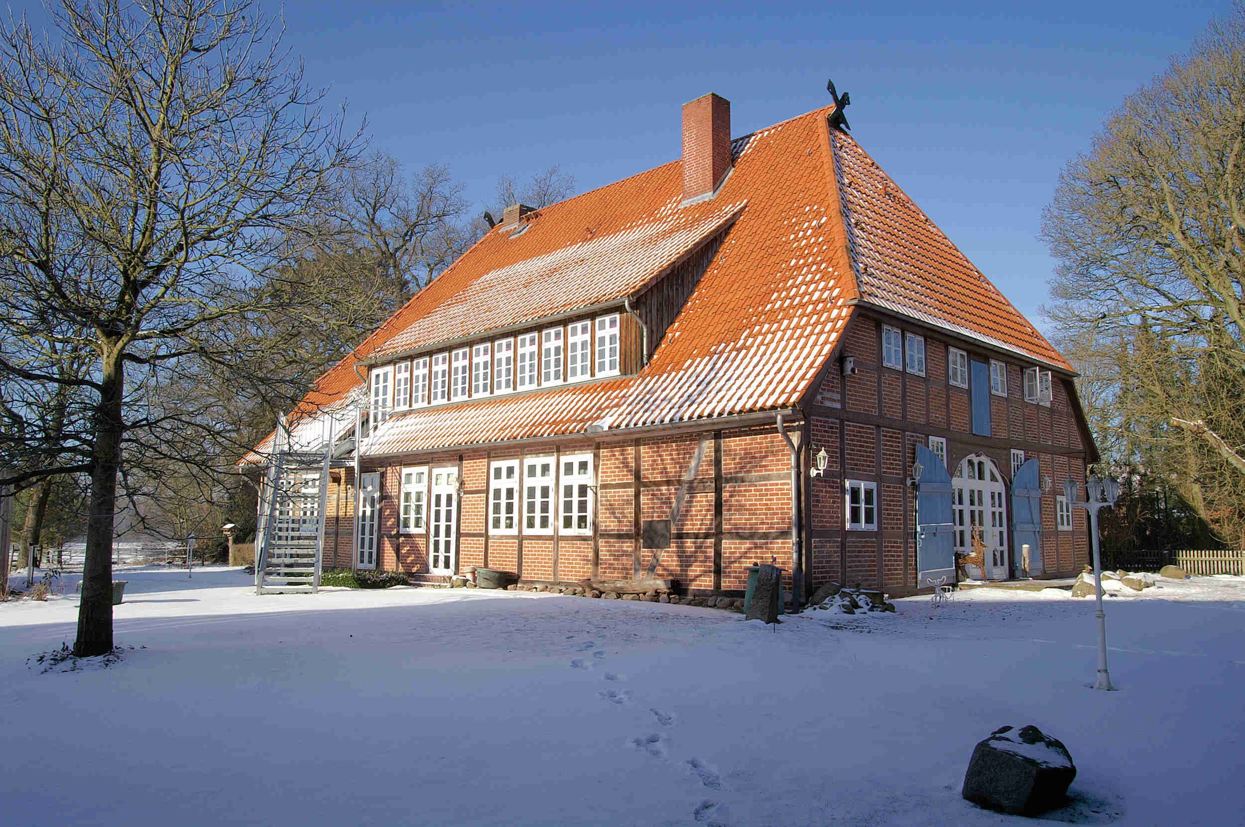 A traditional brick house with a steeply pitched red-tiled roof, surrounded by snow.