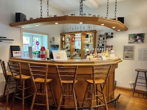 A bar area with wooden stools, a counter with various bottles, and a hanging light fixture.