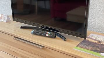 Ein Fernseher auf einer Holzkommode, neben ihm eine Fernbedienung und ein Buch.