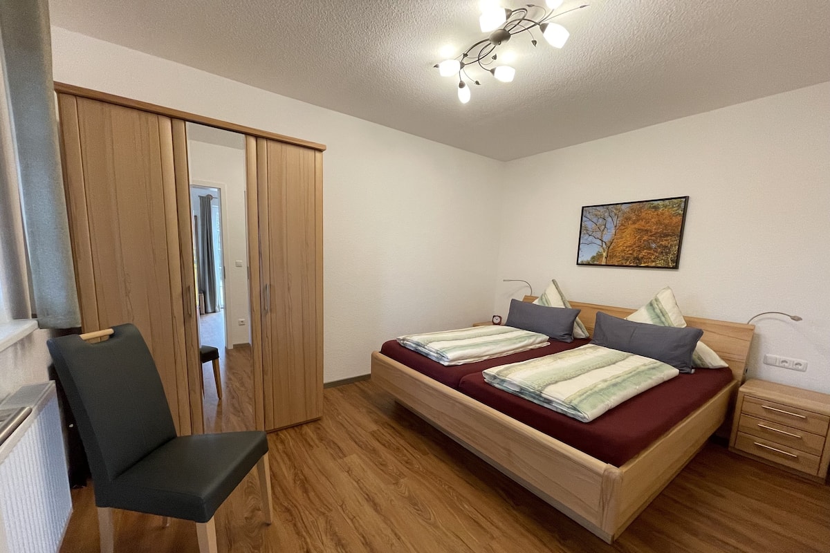 A bedroom with a bed, a chair, a wardrobe, and a nightstand.
