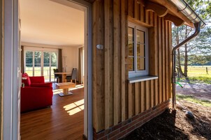 Una cabaña de madera con comedor, un sofá rojo y ventana con vista a un jardín.