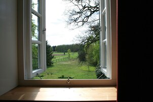 Una ventana con vistas a un campo cubierto de hierba y árboles.