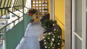 Ein Balkon mit gelber Wand, Blumentöpfen und Korbmöbeln.