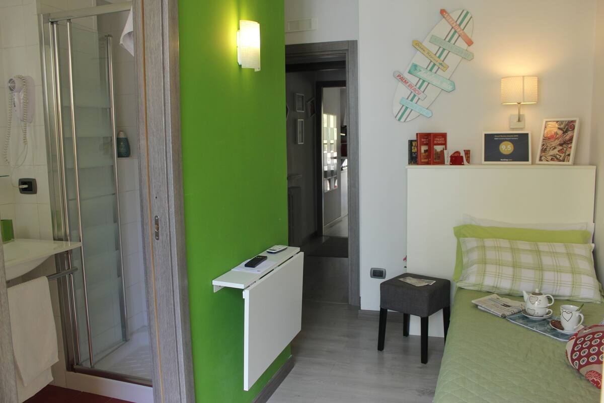 Une chambre d’hôtel avec une douche, un mur d’accent vert, un lit avec une petite table d’appoint et une petite table avec une tasse et une soucoupe.