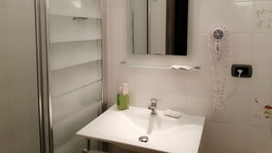 Ein modernes Badezimmer mit Duschkabine aus Glas, einem weißen Waschbecken mit Spiegel darüber und einem an der Wand befestigten Fön.