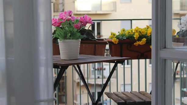 Ein Balkon mit Tisch, Blumentöpfen, einer Bank und einem Geländer.