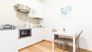 Une cuisine moderne équipée d’un grille-pain, d’un four à micro-ondes et d’une bouilloire. On y trouve une table à manger avec deux chaises et une petite plante en pot.