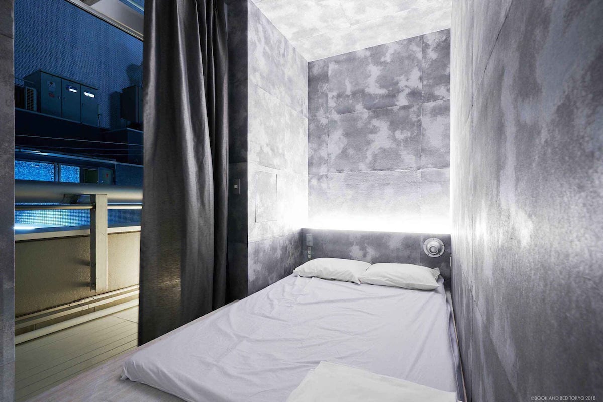 Una habitación de hotel moderna con una cama, un ventanal con cortinas y vistas al exterior.