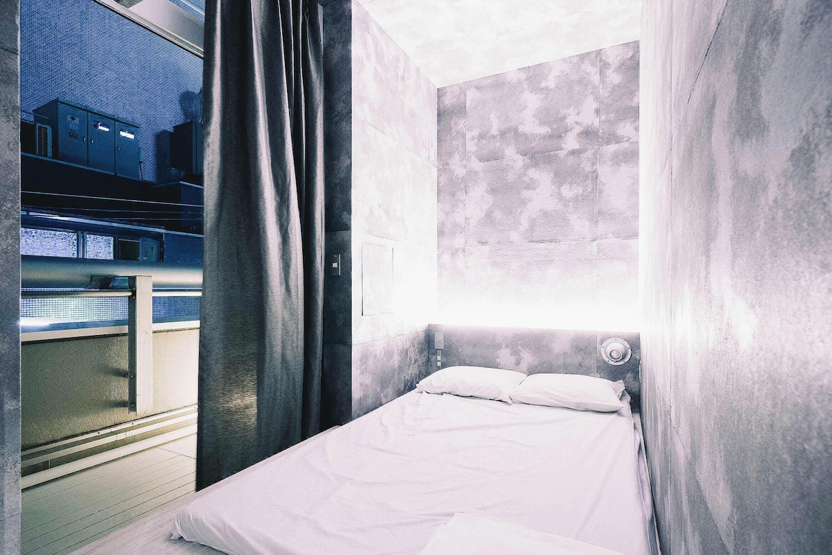 A room with a bed, a window with curtains, and a view of a building outside.