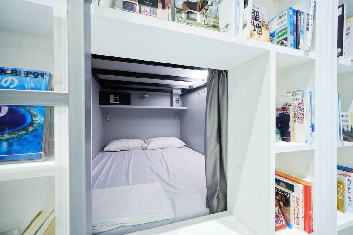 Habitación pequeña con literas, un estante con libros y una ventana que da al océano.