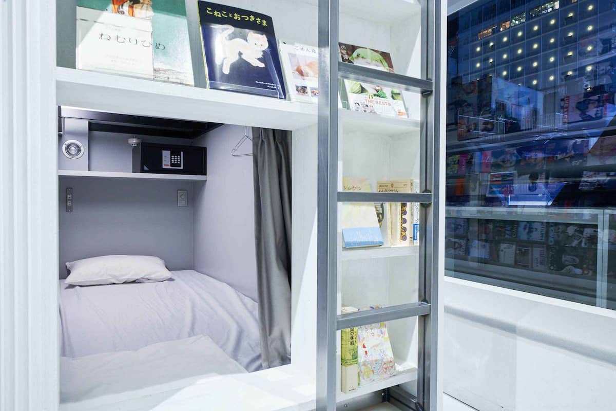 Habitación de hotel compacta con una cama, un escritorio pequeño y una estantería.