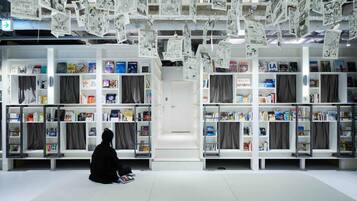 A library with bookshelves filled with books and magazines, a person sitting on the floor, and a white door in the center.