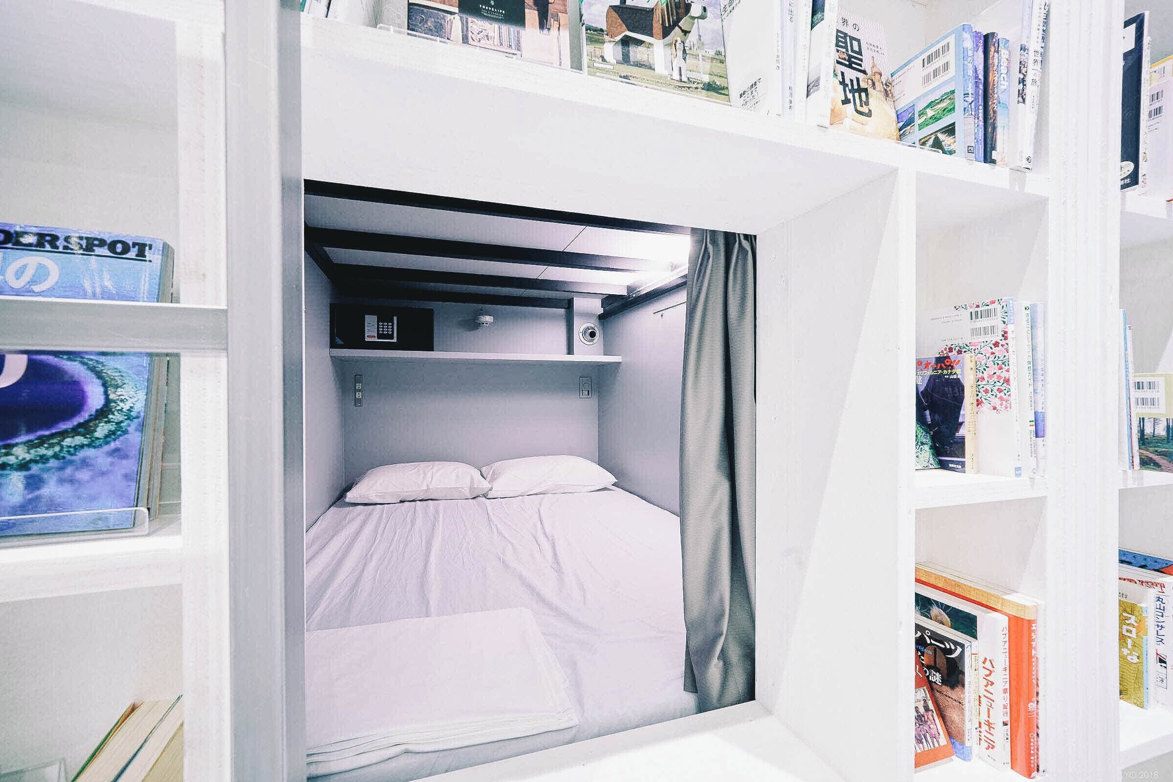 A compact room with a bunk bed, a small shelf with books, and a window with a view of a body of water.