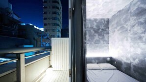 Habitació d'hotel moderna amb balcó, un llit i vista a la ciutat de nit.