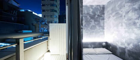 A modern hotel room with a balcony, a bed, and a view of the cityscape at night.