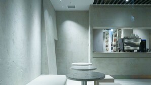 Un interior modern amb disseny minimalista, que inclou una zona de seients amb una taula rodona i tres taules més petites, i una barra amb una màquina de cafè.