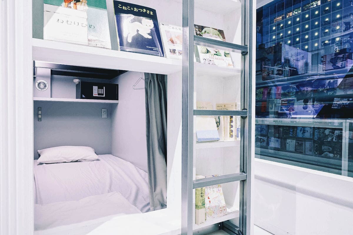 Una habitación compacta con una cama litera, un escritorio pequeño con un ordenador y una pared de cristal que exhibe diversos objetos.