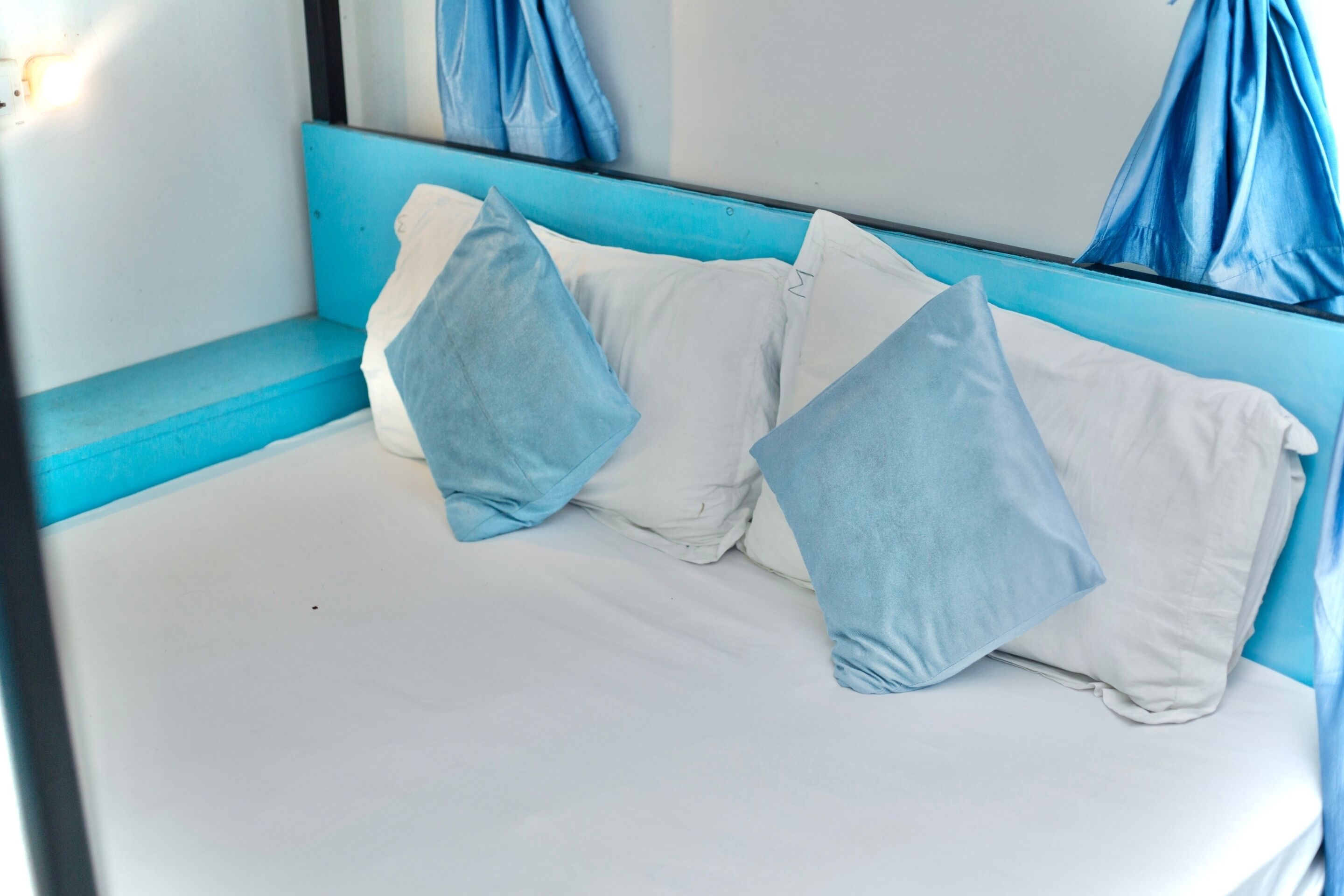 A bed with white sheets and blue pillows, a blue headboard, and a light blue wall.