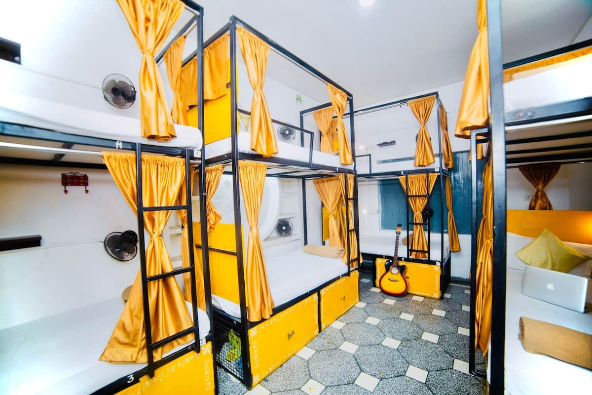 A dormitory room with bunk beds, a small desk, a guitar, and a laptop on a white sofa.