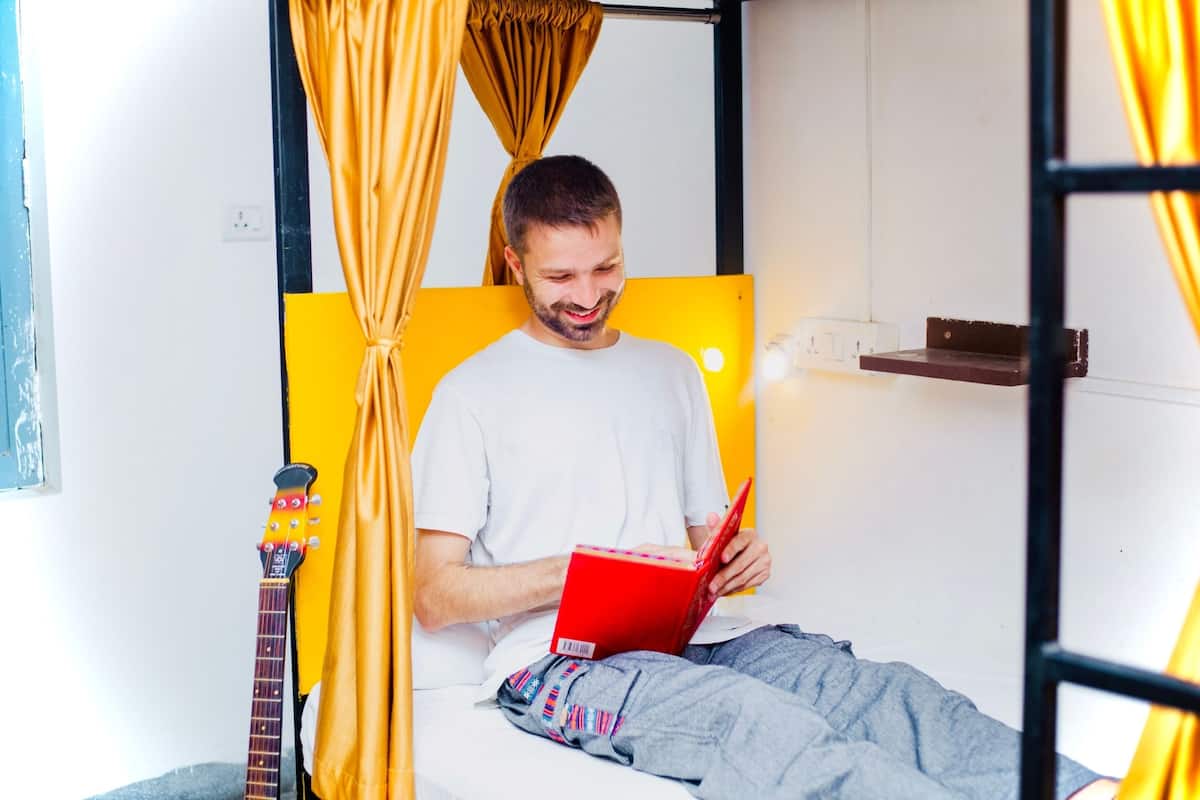 A person sitting on a bed with a guitar, reading a book.
