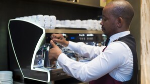 Eine Barista bereitet in einer gewerblichen Umgebung Kaffee mit einer Espressomaschine und Stapeln von Einwegbechern zu.