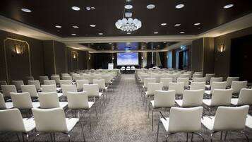 A conference room with rows of white chairs and a large screen at the front.